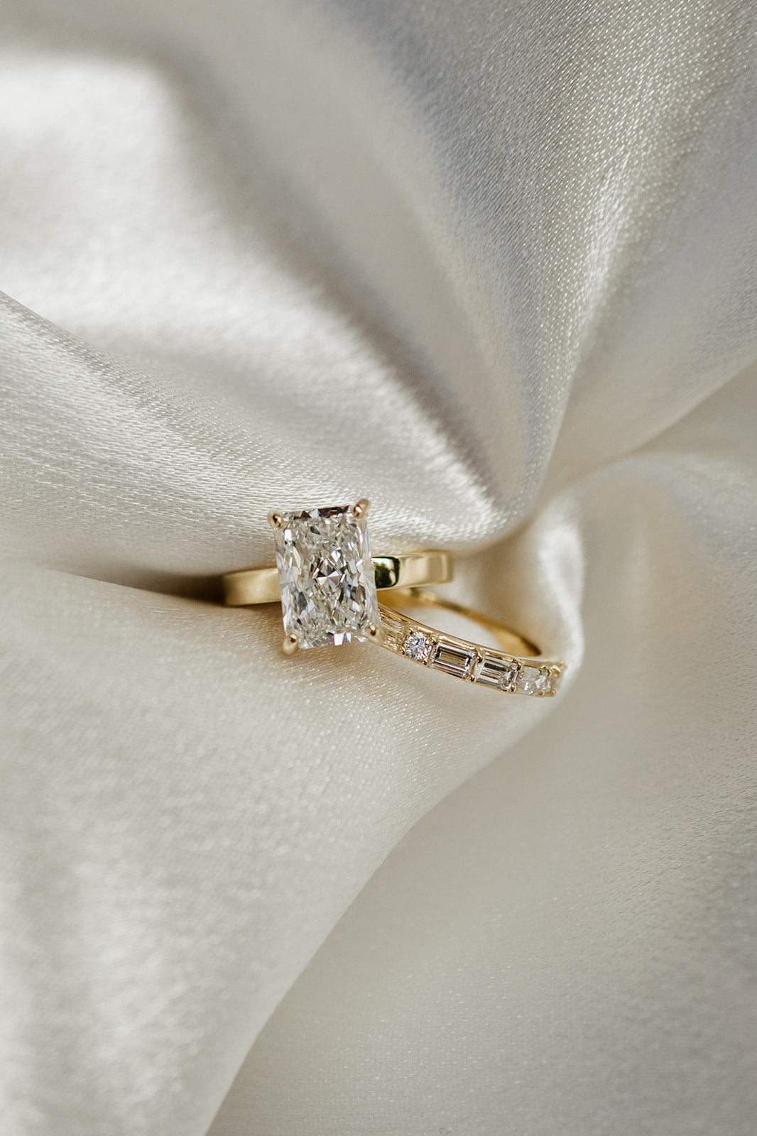 Radiant engagement ring on gold band next to a gold wedding band with round and baguette stones