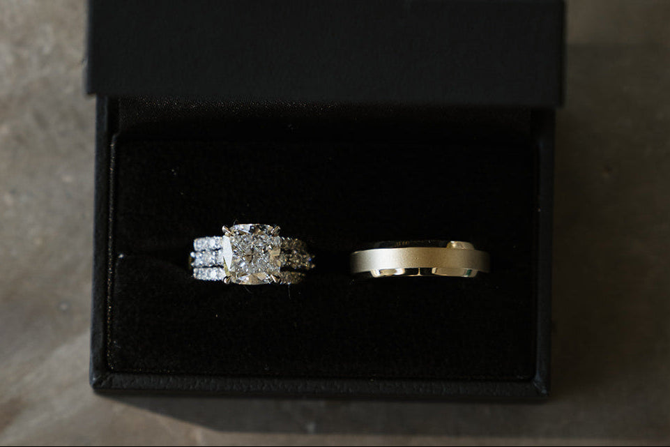 14k white gold setting featuring a Lab Cushion diamond ring 5.02ct E VVS2. Next to a 14K yellow gold, 6 mm Lightweight Beveled-Edge Comfort-Fit Flat Band with Matte Finish